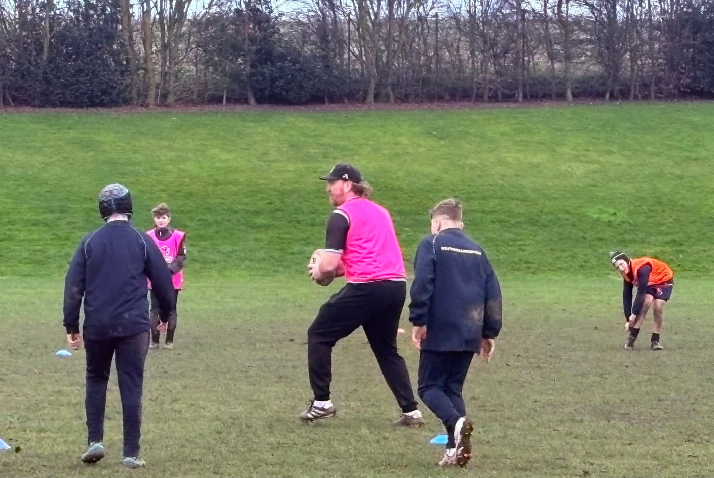 Andy Powell in a pink bib, ball in hand, running a drill with young players